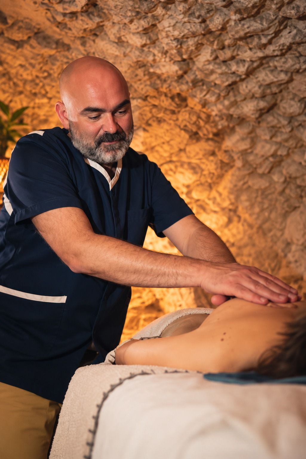 Sébastien Ferrus pendant un massage du dos, devant un mur de pierre éclairé à la bougie